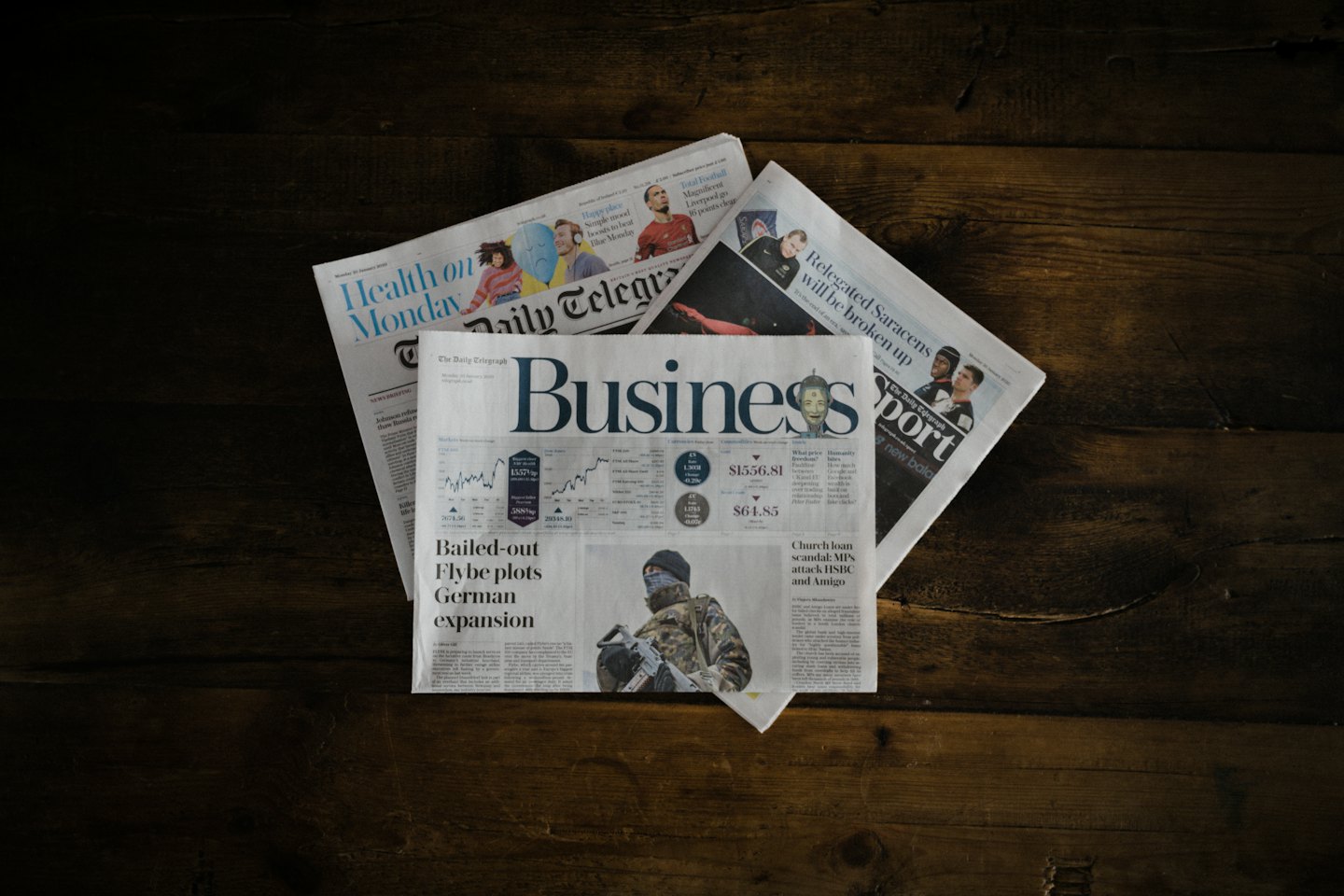 Three overlapping newspapers on a rustic wooden table.
